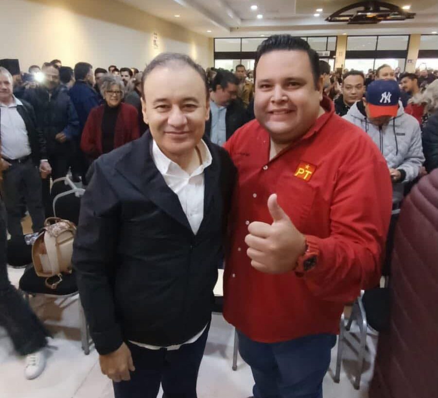 Dos asistentes posan durante un encuentro político en Hermosillo; uno viste una camisa roja con el emblema del PT